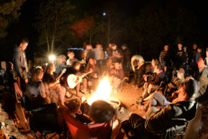 A group of young adults sit around a campfire.
